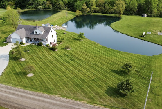 Aerial view of a large Fine Line Lawn Care property with striped mowing pattern and pond